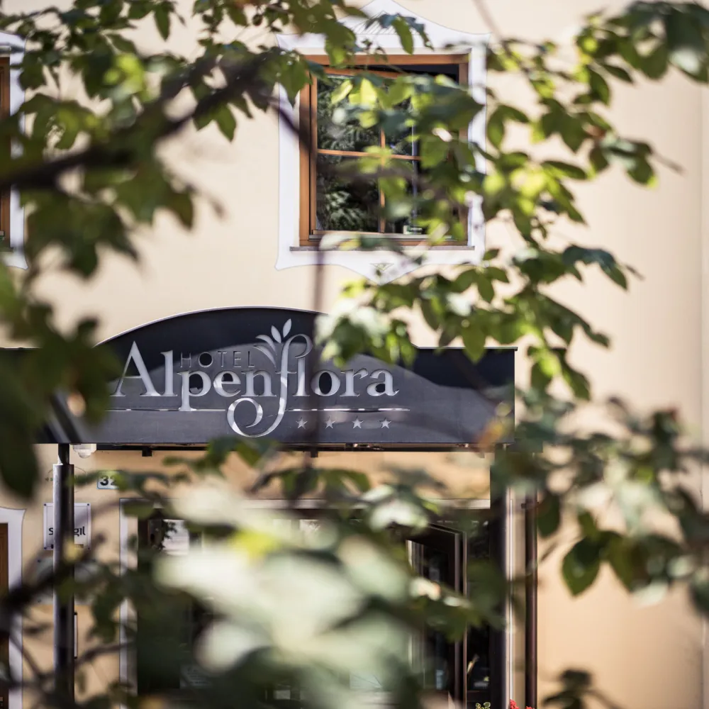 Facciata dell'Hotel Alpenflora con insegna incorniciata da foglie verdi