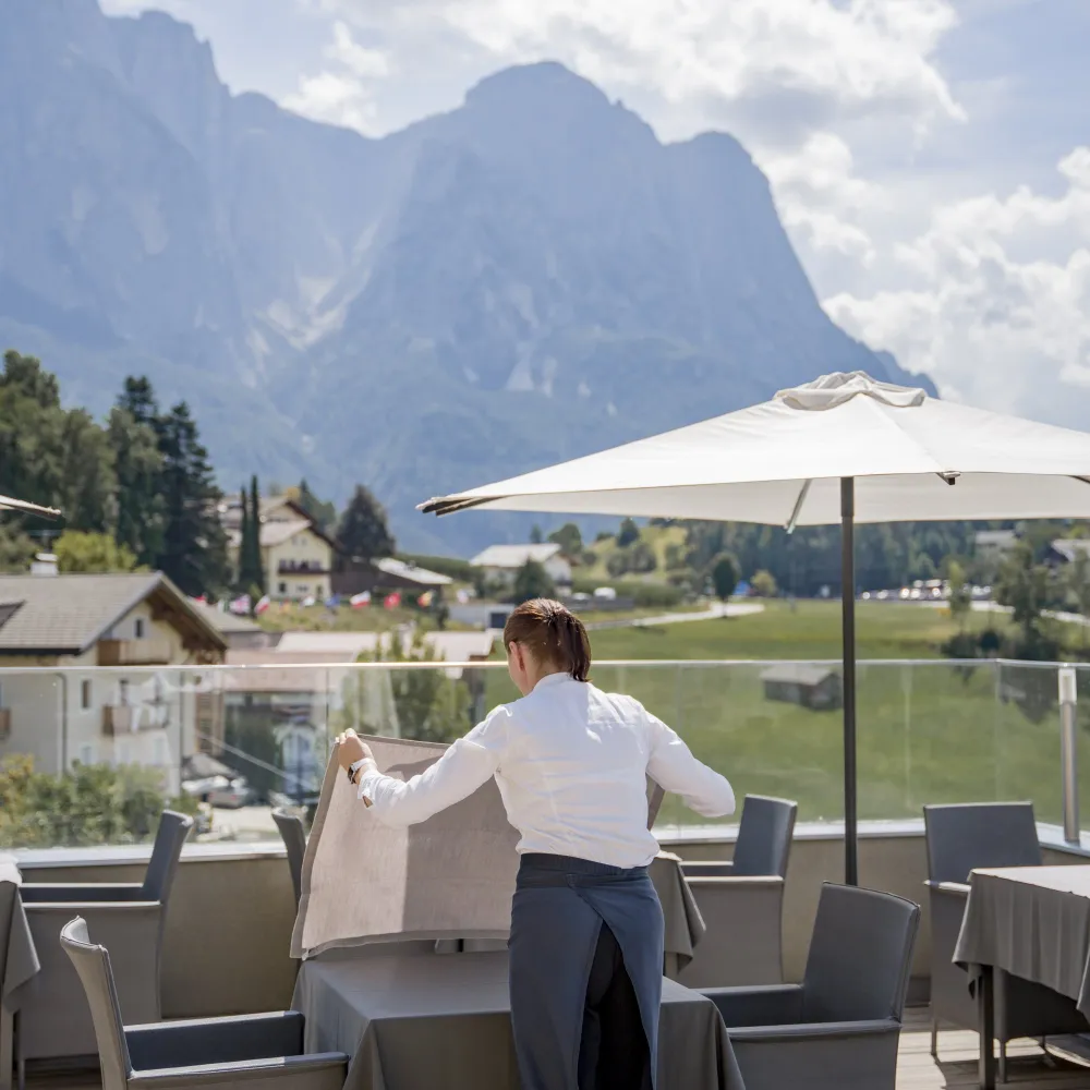 Servicemitarbeiterin deckt einen Tisch auf der Terrasse des Alpenflora mit Blick auf die Dolomiten.