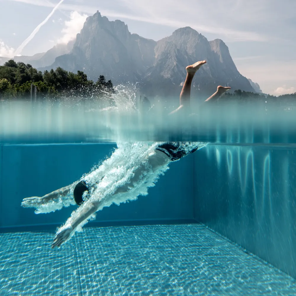Nuotatore nella piscina a sfioro dell'Alpenflora con vista subacquea e lo Sciliar sullo sfondo