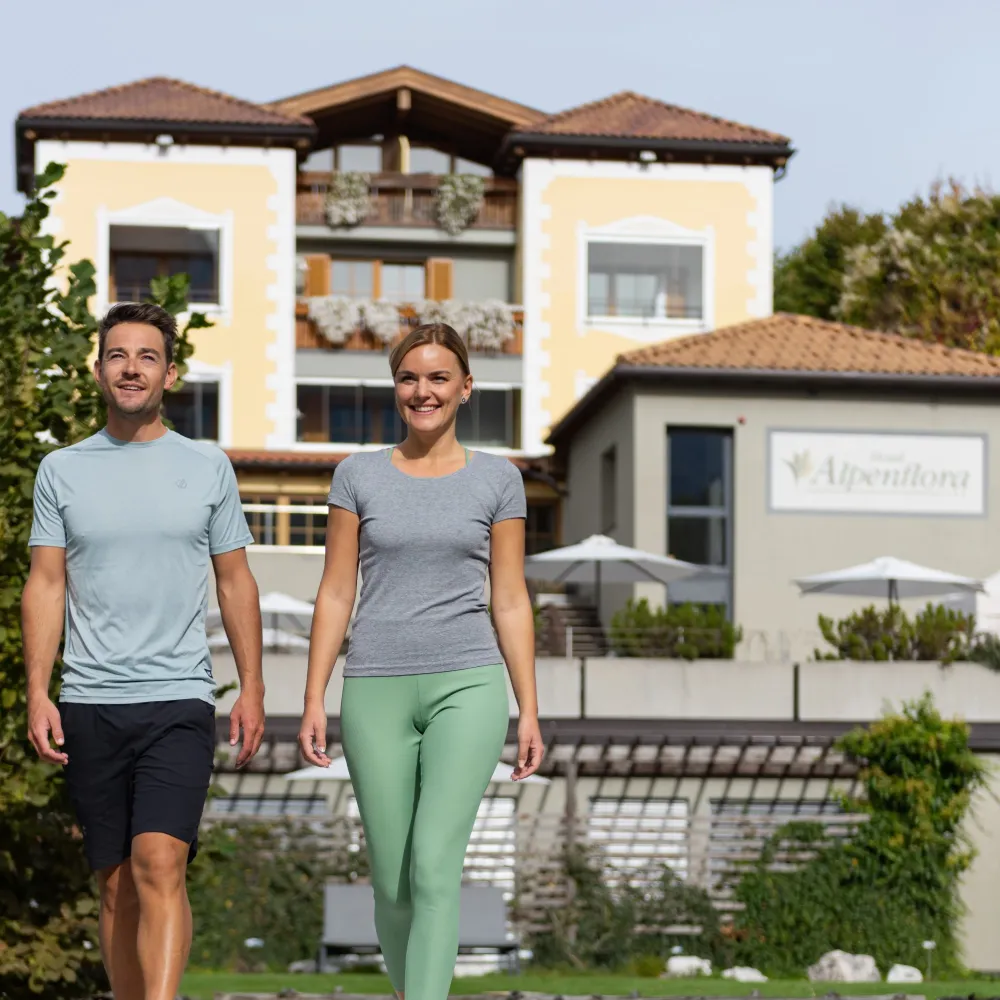 Paar spaziert in Sportkleidung vor der Fassade des Wellnesshotels Alpenflora in Kastelruth.