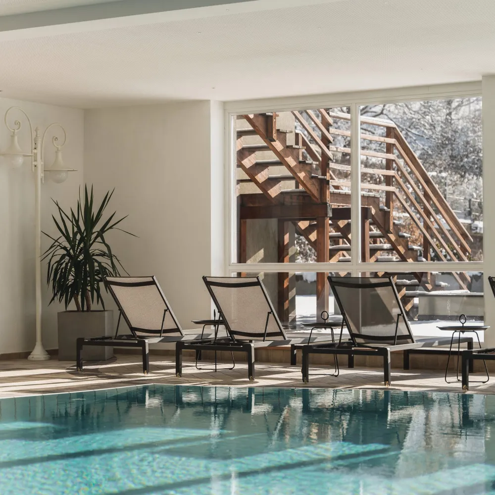 Überdachter Panorama-Pool mit Liegen und Holztreppe im Alpenflora
