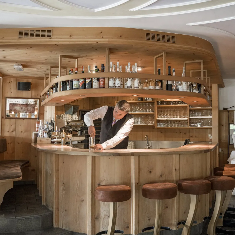 Mitarbeiter an der holzgetäfelten Hotelbar des Wellnesshotels Alpenflora bei der Getränkezubereitung.