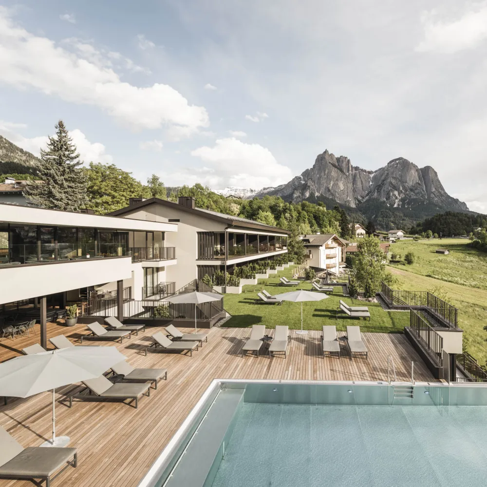 Außenansicht des Wellnesshotels Alpenflora mit Liegeterrasse, Pool und den Dolomiten im Hintergrund.
