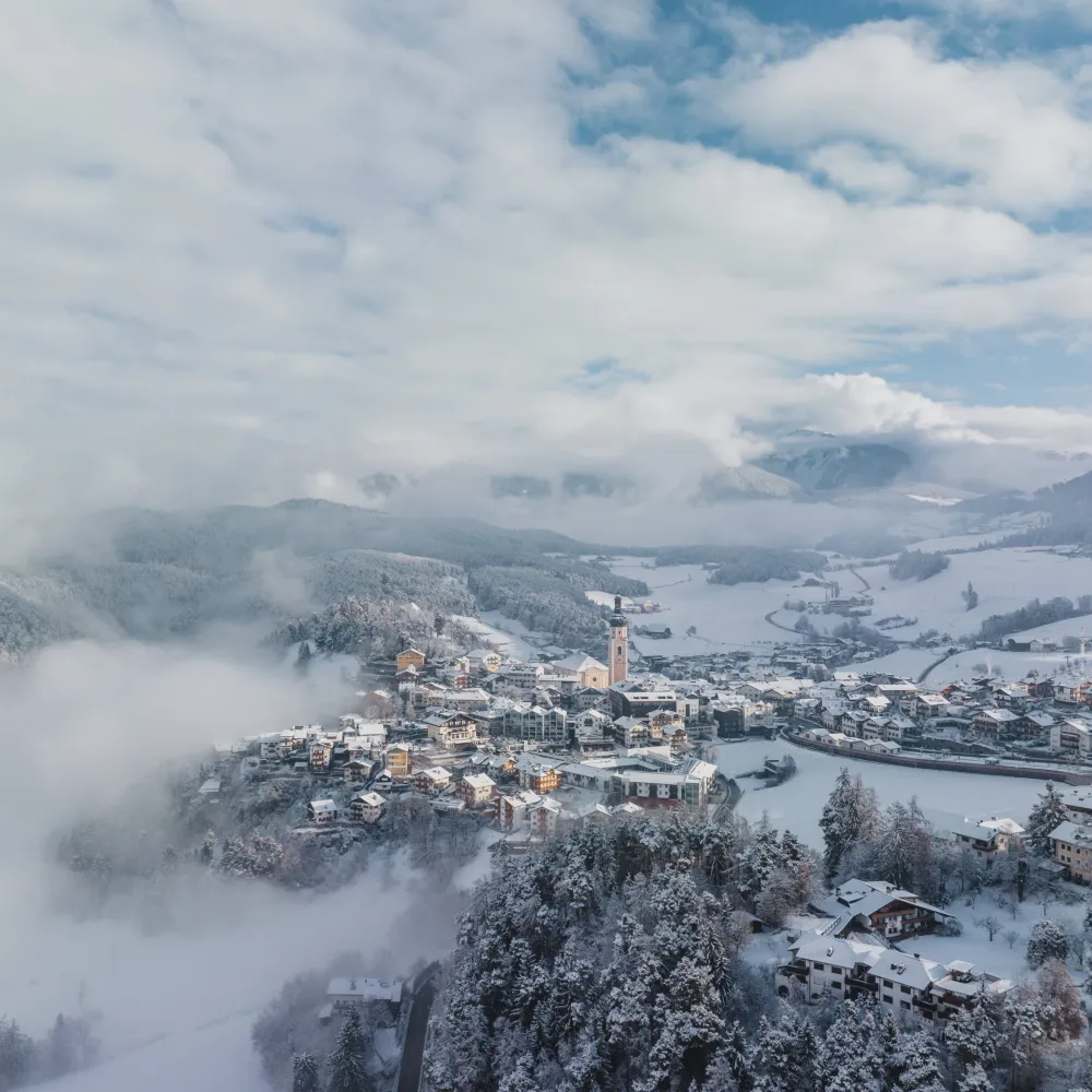 Verschneites Kastelruth aus der Luft mit Kirchturm und Dolomiten im Winter