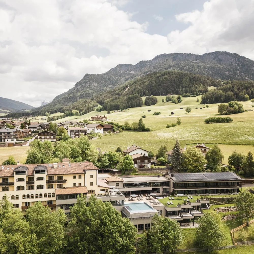 Luftaufnahme des Wellnesshotels Alpenflora mit Pool und Garten in Kastelruth vor Almwiesen.