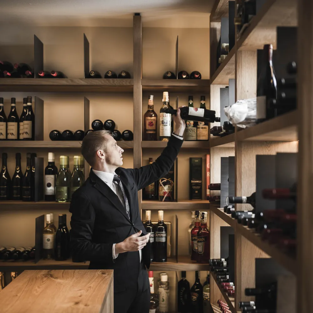 Sommelier wählt am gut gefüllten Weinregal des Alpenflora eine Flasche aus