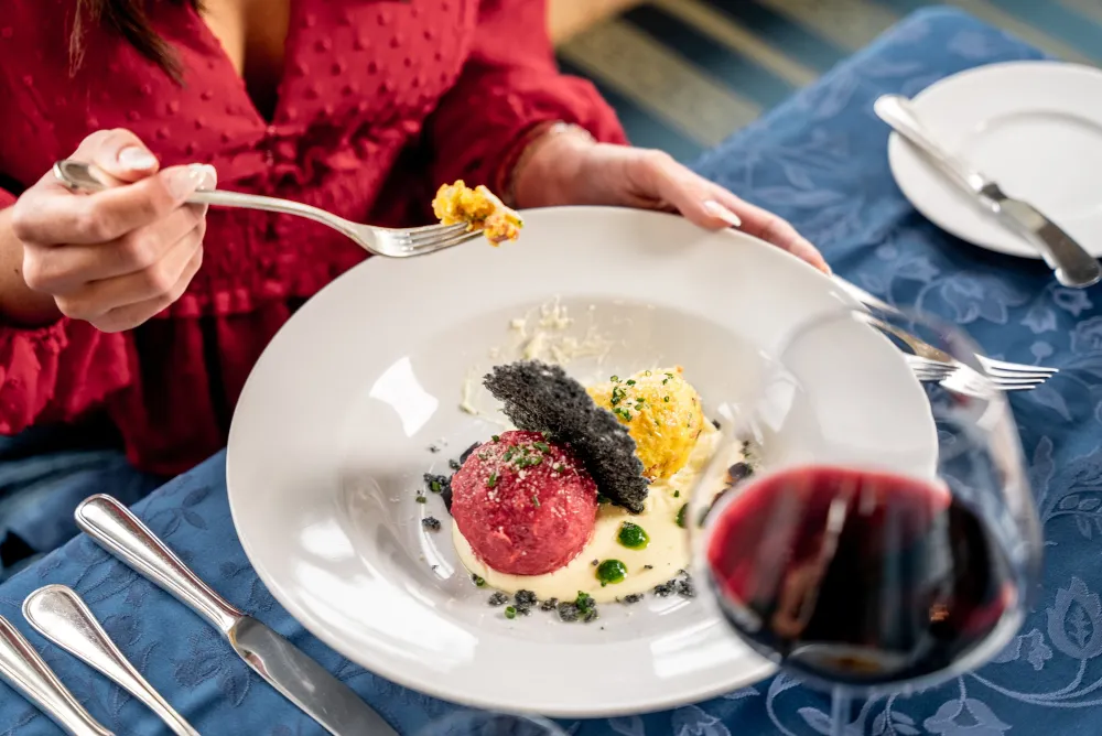 Gast genießt ein fein angerichtetes Rindertatar mit einem Glas Rotwein im Restaurant des Alpenflora