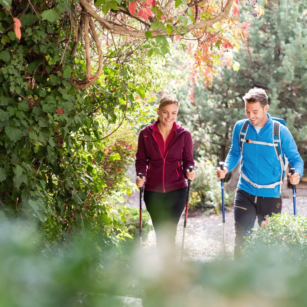 Lächelndes Paar beim Nordic Walking mit Stöcken auf einem Weg durch herbstliches Grün nahe dem Wellnesshotel Alpenflora
