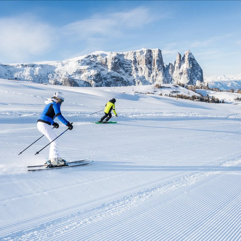 Zwei Skifahrer auf einer frisch präparierten Piste vor der Kulisse der verschneiten Dolomiten