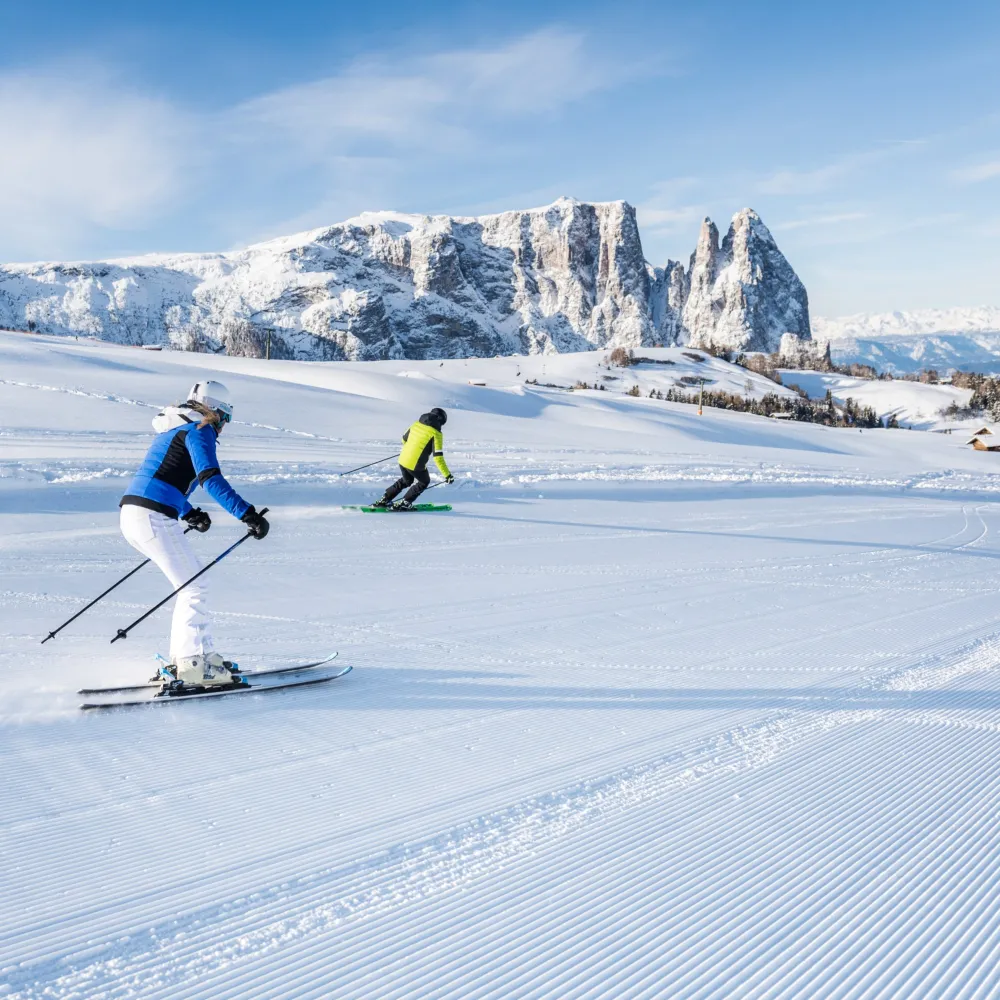 Two skiers on a freshly groomed slope against the backdrop of the snow-covered Dolomites