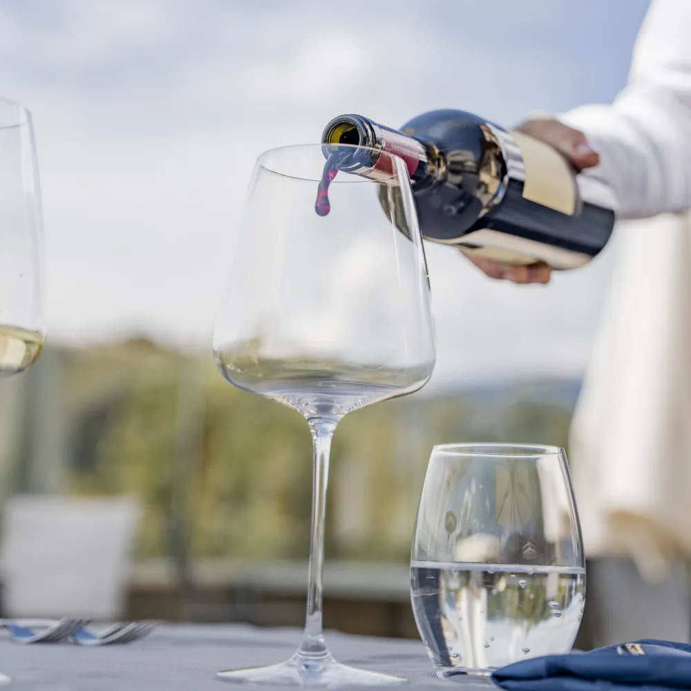 Red wine being poured into the glass, with a glass of water on the Alpenflora terrace
