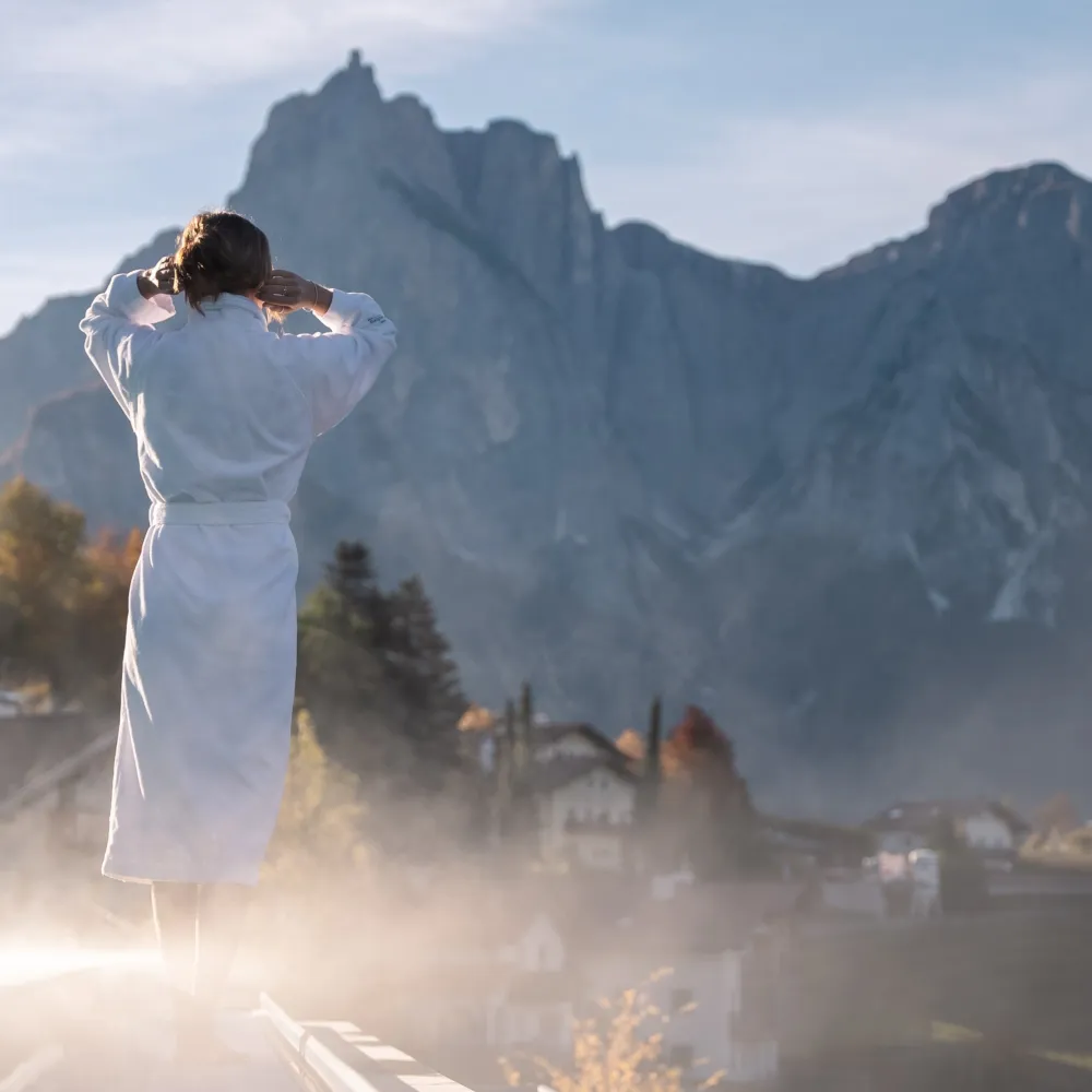 Frau im Bademantel genießt den Blick auf den Schlern am Pool des Wellnesshotels Alpenflora in Kastelruth.