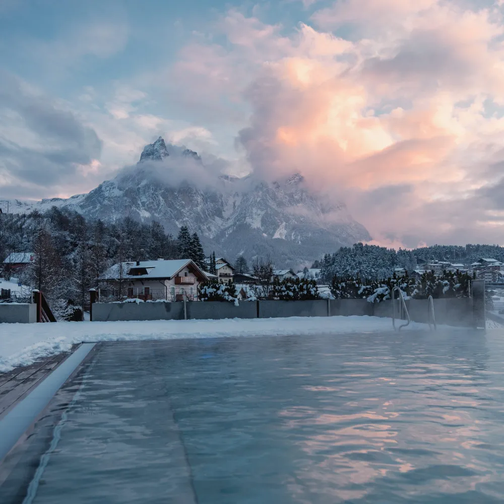 Dampfender Außenpool im Schnee bei Dämmerung mit Blick auf die verschneiten Dolomiten