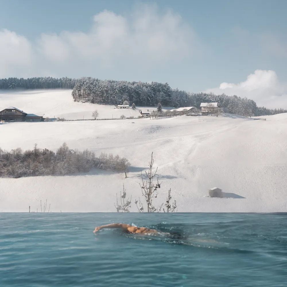 Schwimmer im beheizten Außenpool des Alpenflora vor verschneiter Landschaft
