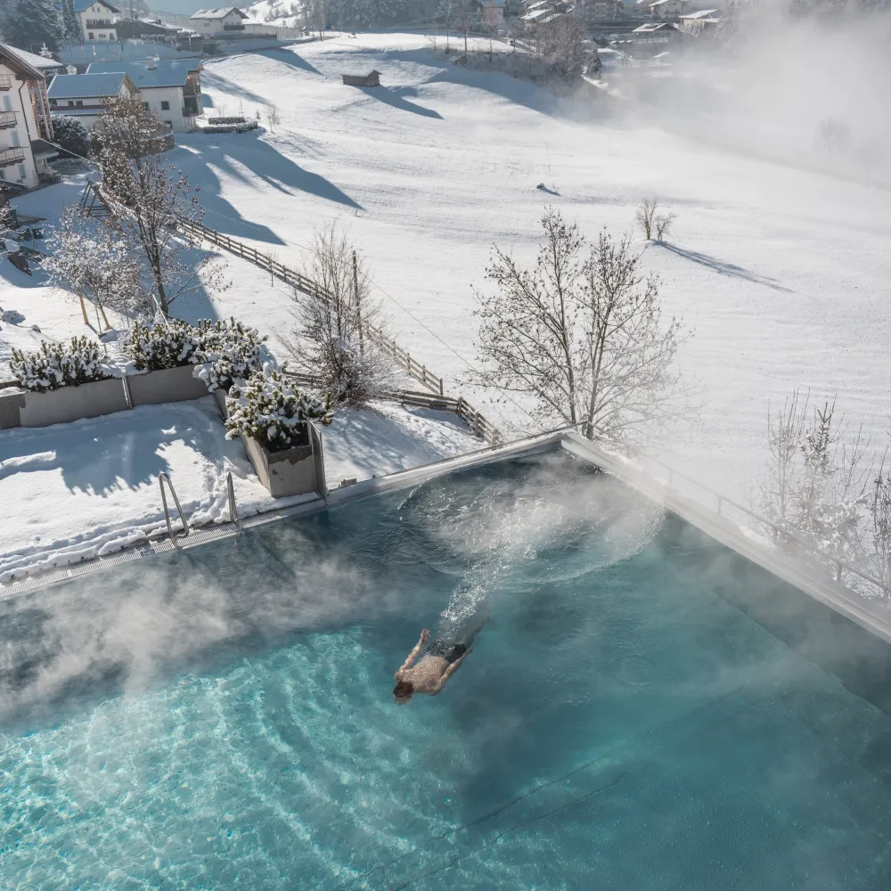 Guest swimming in the steaming outdoor pool with snowy slopes and houses in the background.