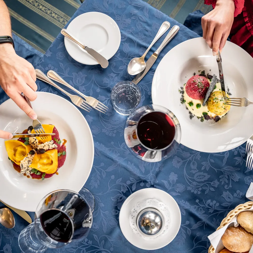 Two guests enjoying South Tyrolean dishes and red wine at a laid table at the Alpenflora