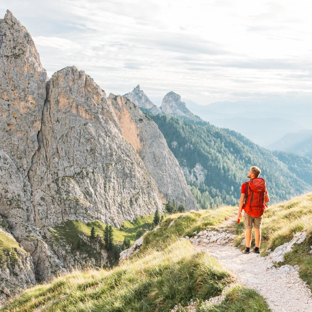 Hiker with a red backpack on a mountain trail in the Dolomites near Castelrotto