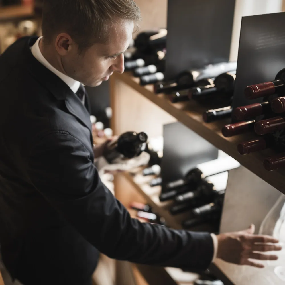 Alpenflora sommelier reaching for a bottle from the dark wine shelves