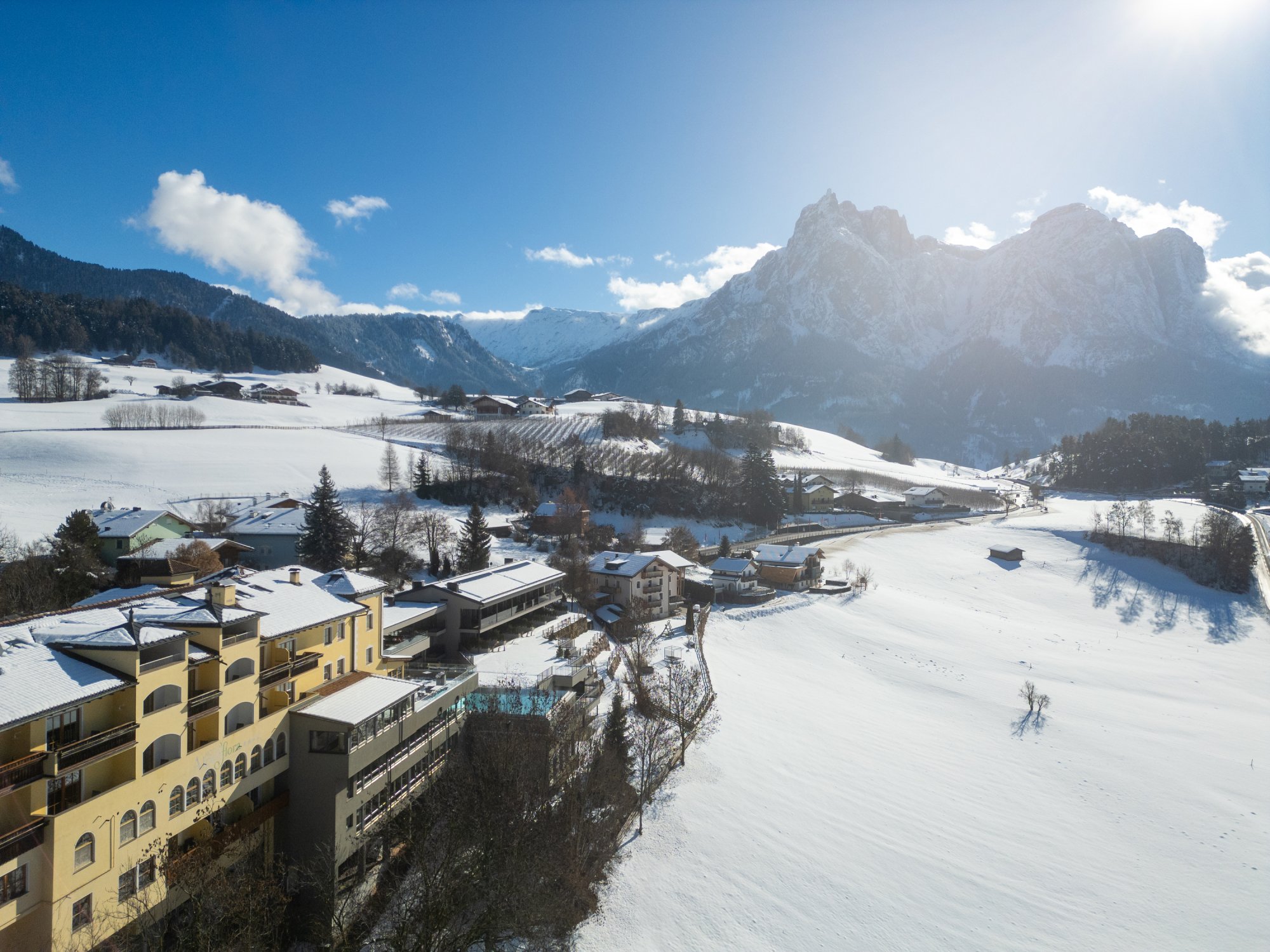 Wellnesshotel Alpenflora in winter with snowy landscape, balconies and mountain panorama under a blue sky.