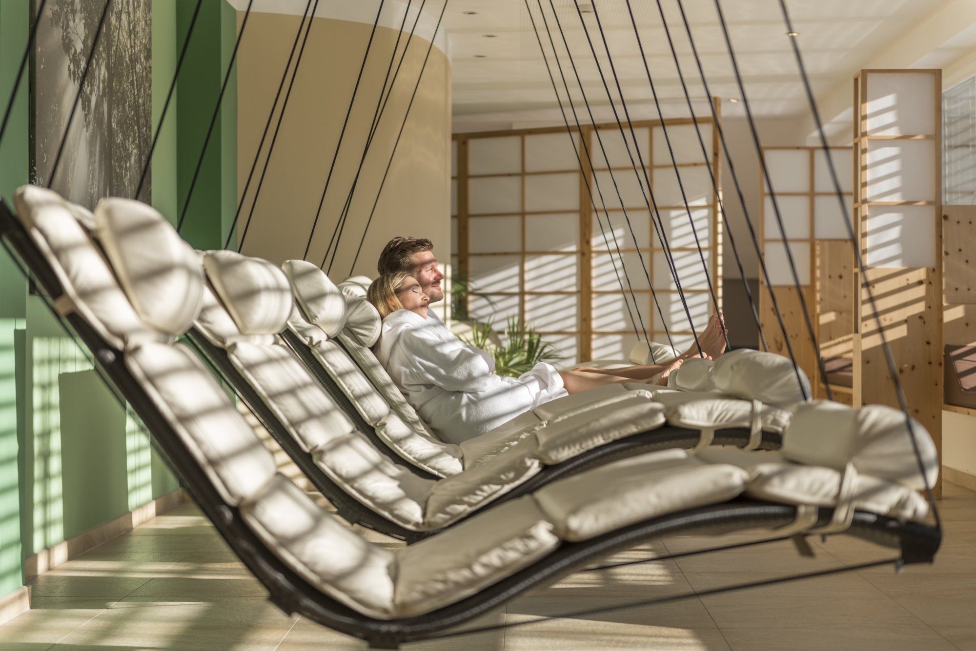 Guest in a bathrobe relaxing on a suspended lounger in the bright relaxation area of the hotel.