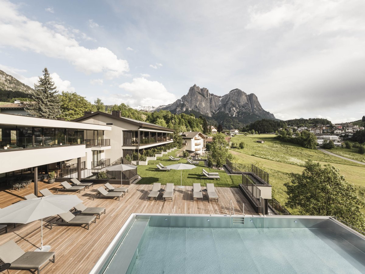 Vista estiva dell'Hotel Alpenflora con terrazza solarium, piscina e vista sullo Sciliar