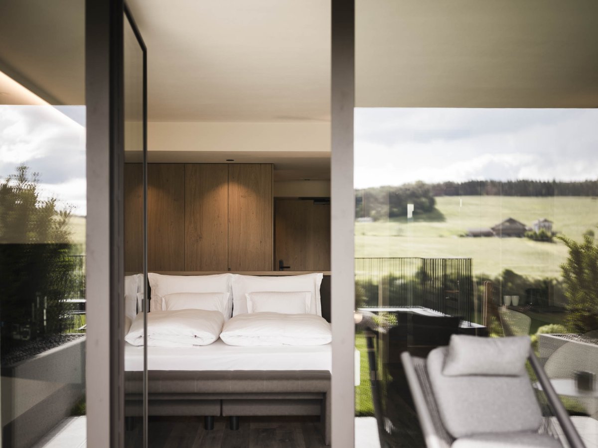 Camera con letto matrimoniale, elementi in legno e finestra panoramica sui prati vicino a Castelrotto