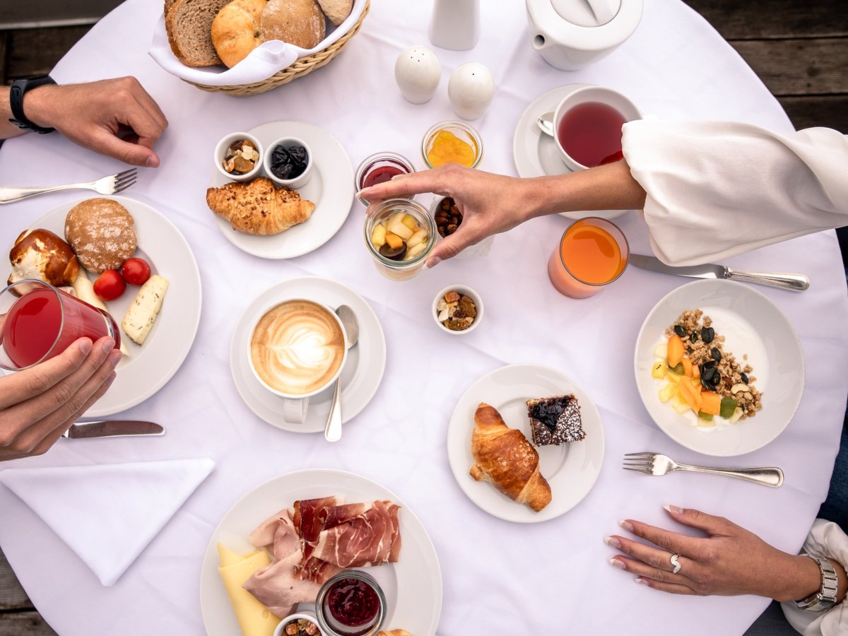 Tavola della colazione vista dall'alto con cappuccino, croissant, formaggio e speck altoatesino
