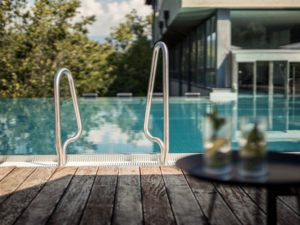 Scaletta in acciaio della piscina esterna con deck in legno e bevande all'Hotel Alpenflora