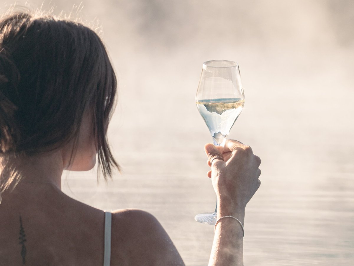 Frau entspannt im dampfenden Außenpool und hält ein Glas Weißwein in der Hand.
