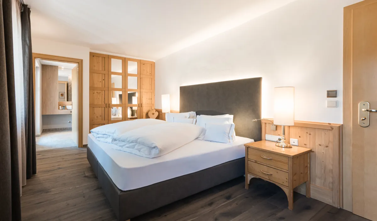 Doppelzimmer Classic im Wellnesshotel Alpenflora mit Doppelbett, Holzschrank mit Glastüren und Durchgang zum Badezimmer.