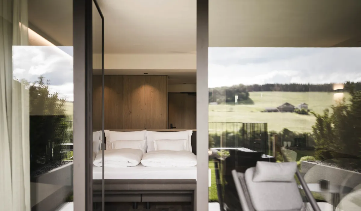 Blick von der Terrasse durch die offene Glastür ins Zimmer Garden Relax mit grüner Wiese im Hintergrund im Wellnesshotel Alpenflora.