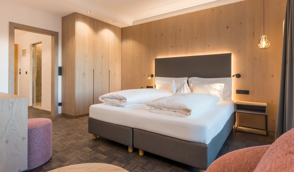 Camera doppia Panorama nel Wellnesshotel Alpenflora con letto matrimoniale, armadio in legno, rivestimento in legno e pouf rosa.