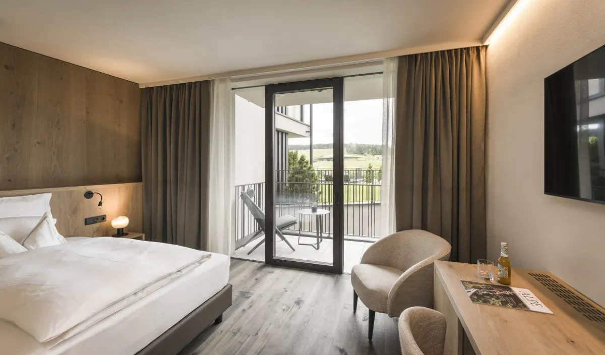 Camera singola Garden Single Stay nel Wellnesshotel Alpenflora con letto, poltrona, scrivania e balcone con vista sul verde.