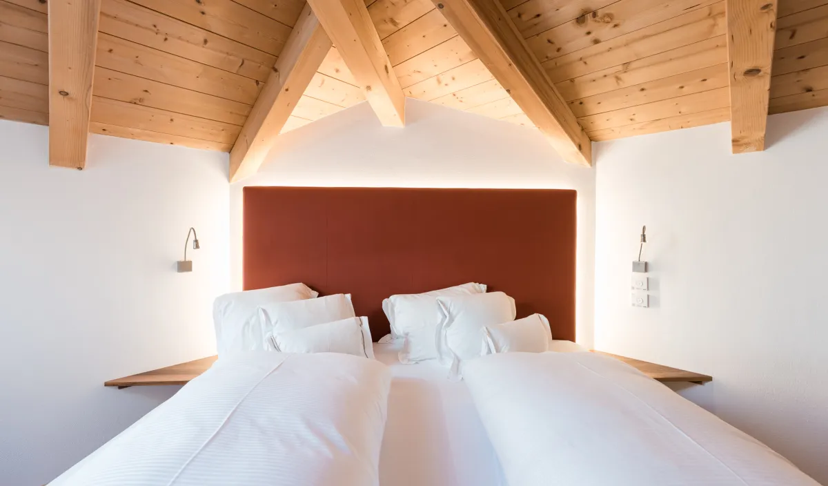 Doppelbett mit terracottafarbenem Kopfteil, indirekter Beleuchtung und Holzbalkendecke im Doppelzimmer Attico.