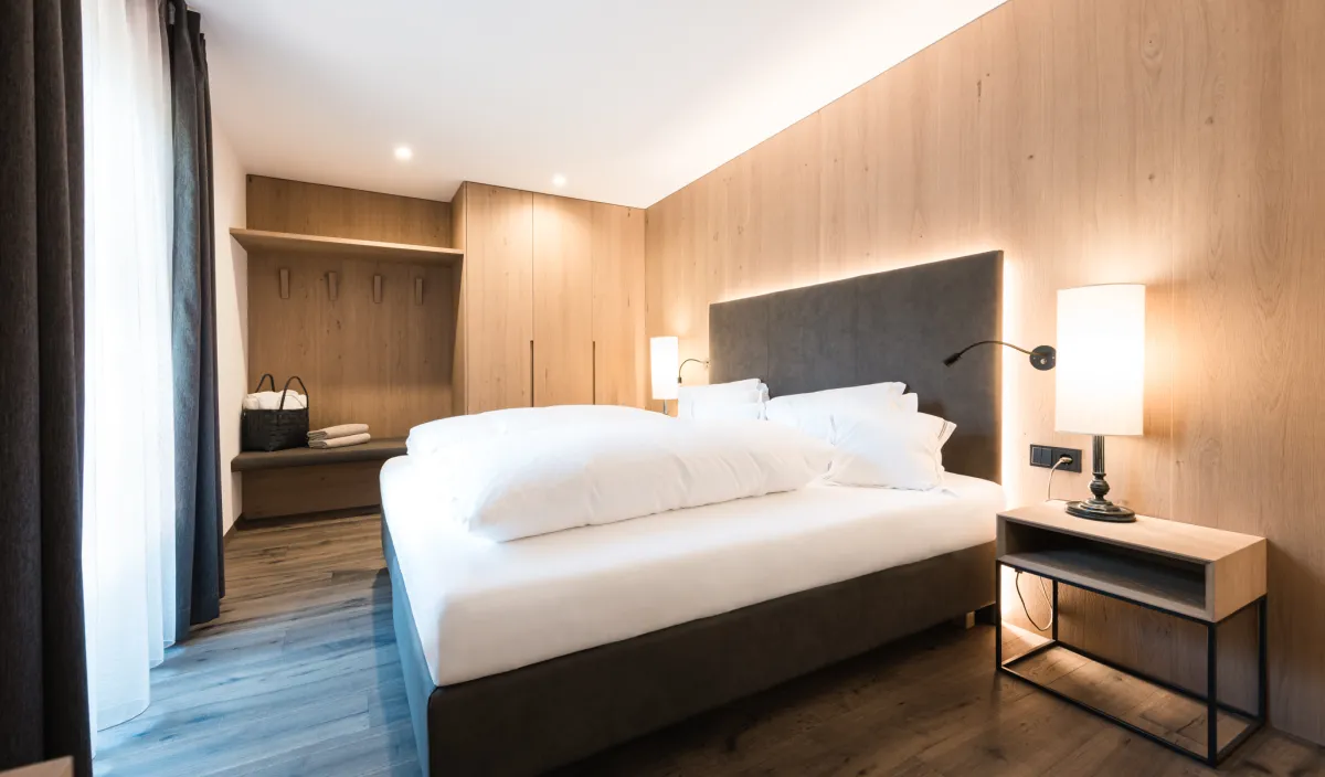Doppelzimmer Classic im Wellnesshotel Alpenflora mit Doppelbett, Holzwandverkleidung, offener Garderobe und Nachttisch.