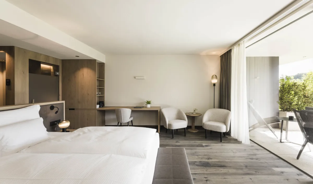 Helles Doppelzimmer Garden Relax mit Doppelbett, Schreibtisch, zwei Sesseln und offenem Zugang zur Terrasse.