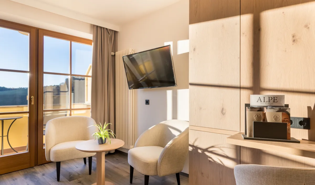 Sitzecke mit zwei Sesseln, Beistelltisch und Fernseher neben der Balkontür im Zimmer Panorama Superior.