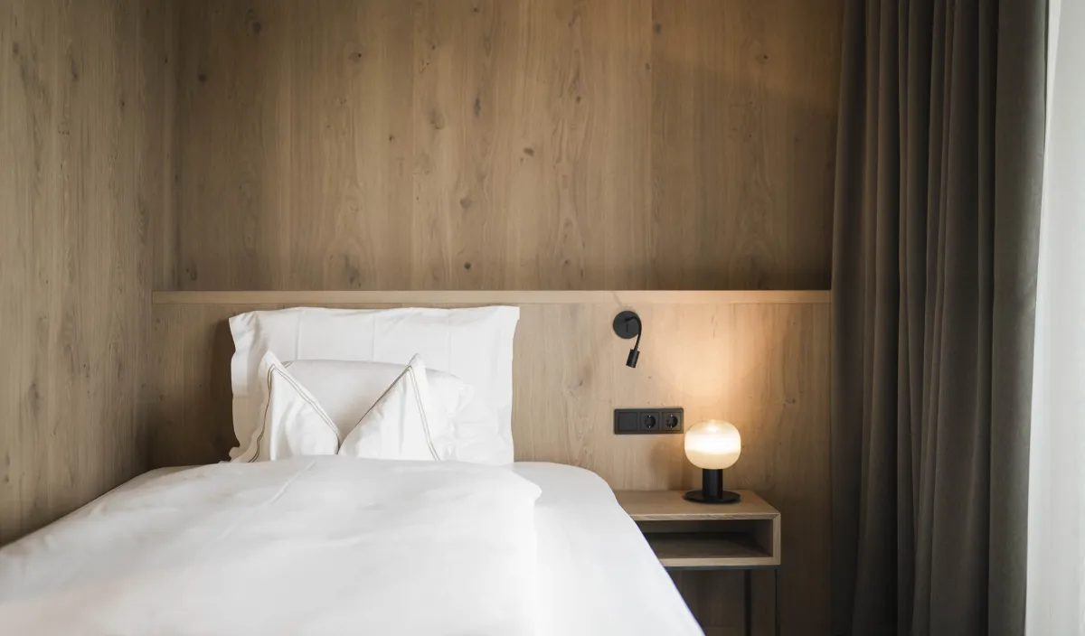 Letto singolo con biancheria bianca, comodino con lampada e rivestimento in legno nella camera Garden Single Stay.