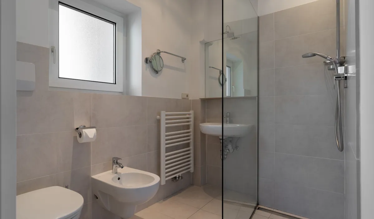 Bagno con doccia in vetro a filo pavimento, WC, bidet, lavabo e scaldasalviette.