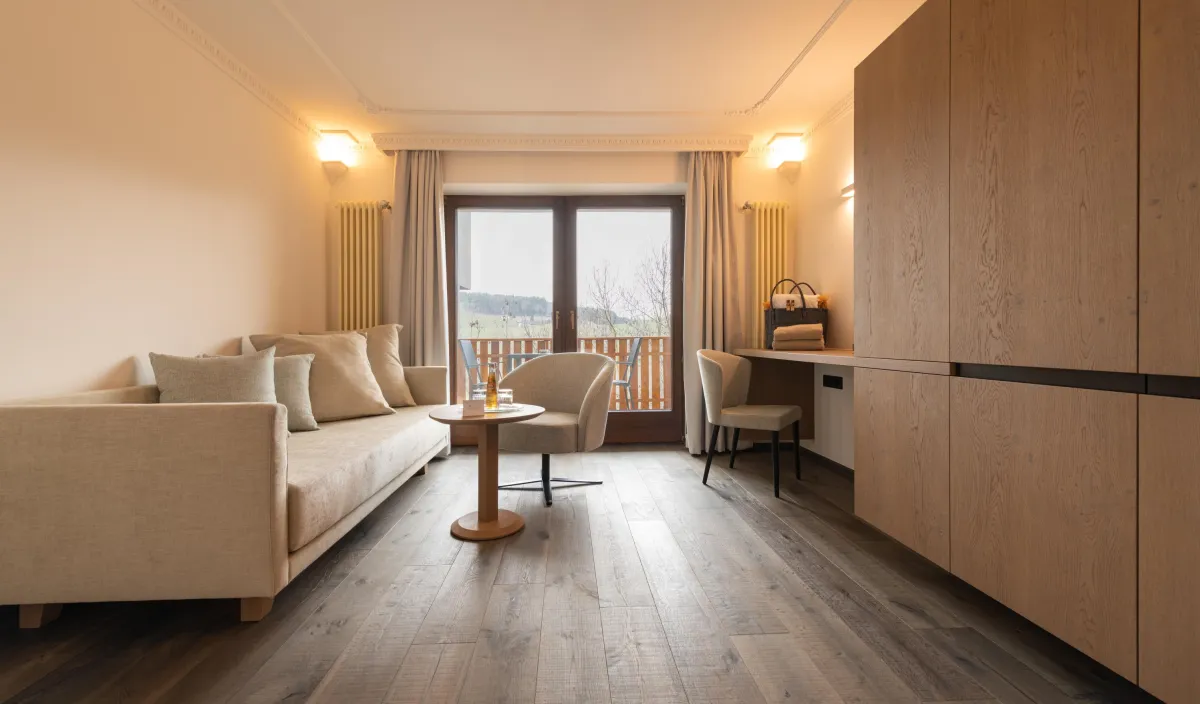 Zona giorno della Sun Suite con divano, poltrona, scrivania e porta del balcone con vista sul verde.