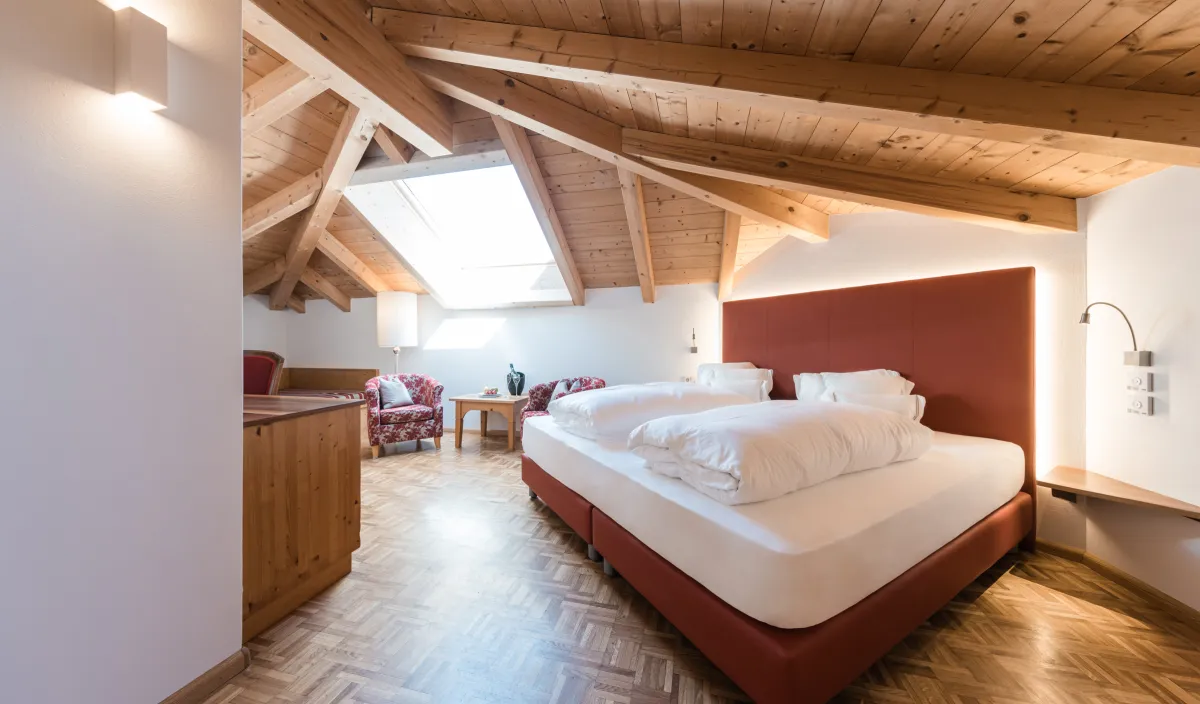 Doppelzimmer Attico mit Doppelbett, Parkettboden, Dachfenster und Sitzecke mit Sesseln und Beistelltisch.