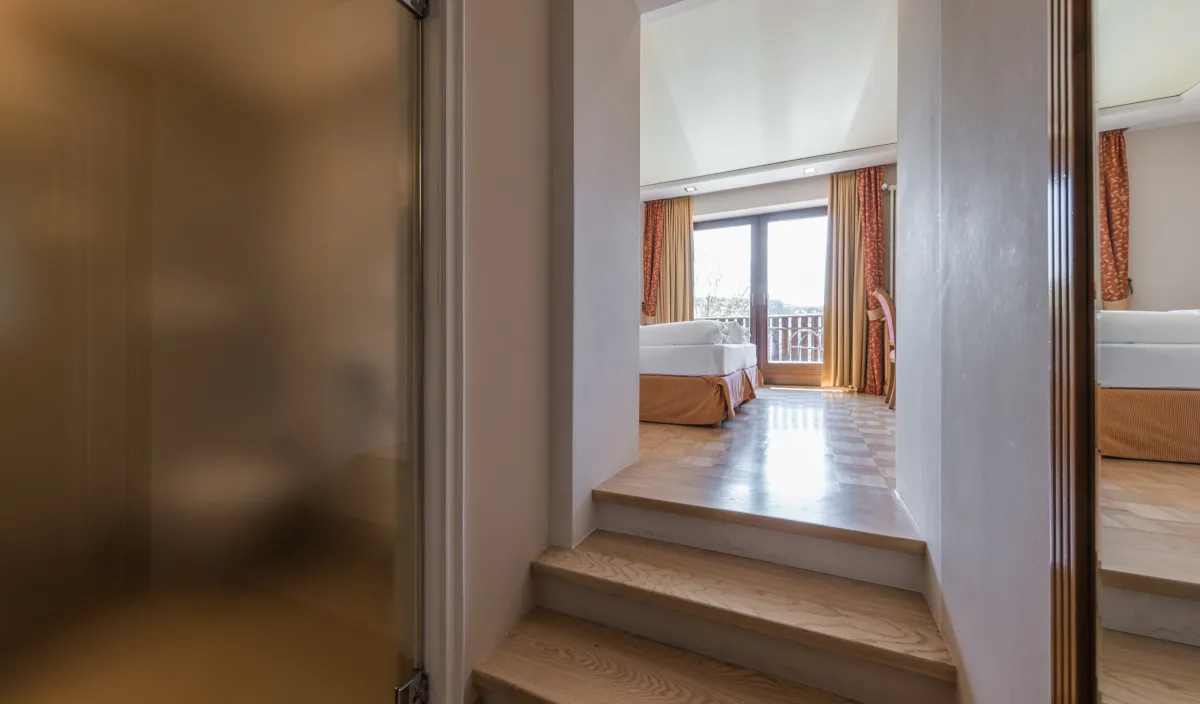 Blick vom Badezimmer über die Stufen in den Schlafbereich mit Doppelbett und Balkontür im Zimmer Sun.