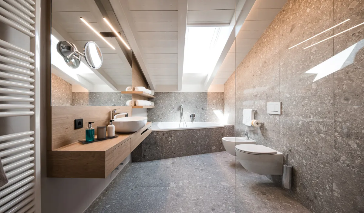 Badezimmer mit Aufsatzwaschbecken auf Holzwaschtisch, Badewanne unter der Dachschräge, WC und Bidet.