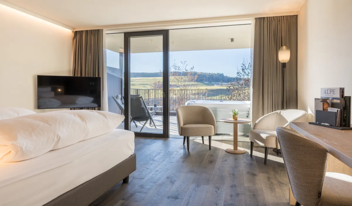 Blick durch das Zimmer Garden Romantic auf die Terrasse mit Whirlpool und Bergpanorama.