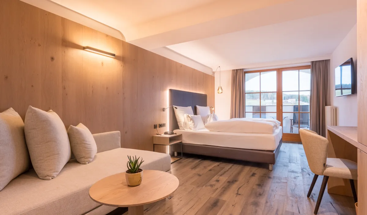 Geräumiges Zimmer Panorama Superior mit Sofa, Doppelbett, Holzwandverkleidung und Balkontür mit Aussicht.