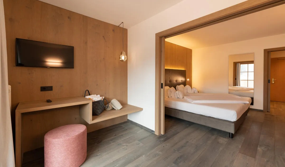 Zona giorno con televisore, consolle, pouf rosa e passaggio alla camera da letto della Sun Suite.