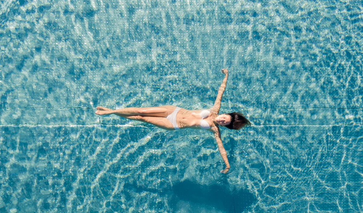 Person schwimmt im türkisfarbenen Pool des Wellnesshotels Alpenflora von oben gesehen