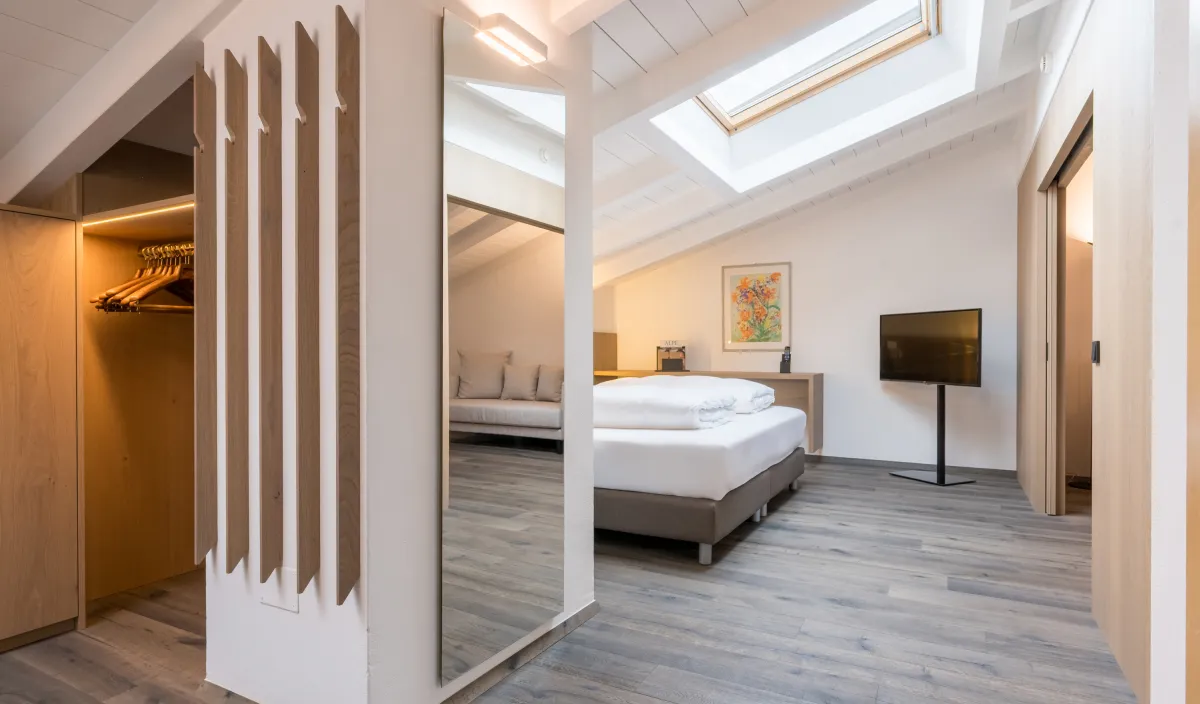 Guardaroba con armadio illuminato e specchio a figura intera, vista sul letto e lucernario dell'Attico Suite.