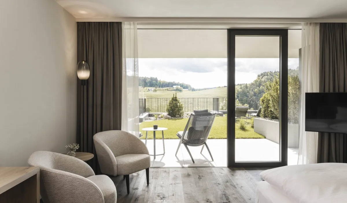 Blick vom Zimmer Garden Relax durch die offene Terrassentür auf den Garten und die grüne Landschaft.