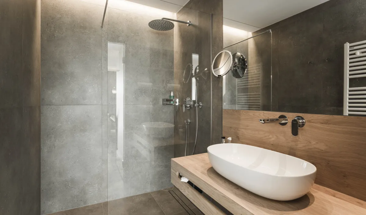 Bagno con doccia a pioggia walk-in, lavabo d'appoggio su mobile in legno e pareti in pietra naturale.